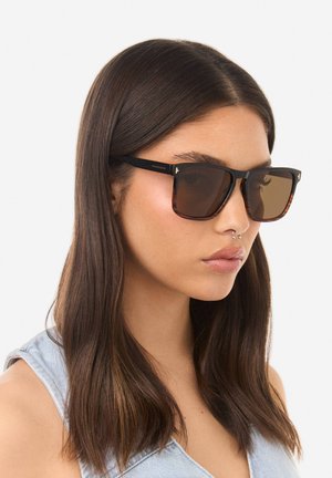 Hnědě tónované sluneční brýle s černým a želví geometrickým rámem. Mají elegantní design s průhlednými kovovými doplňky na stranách.