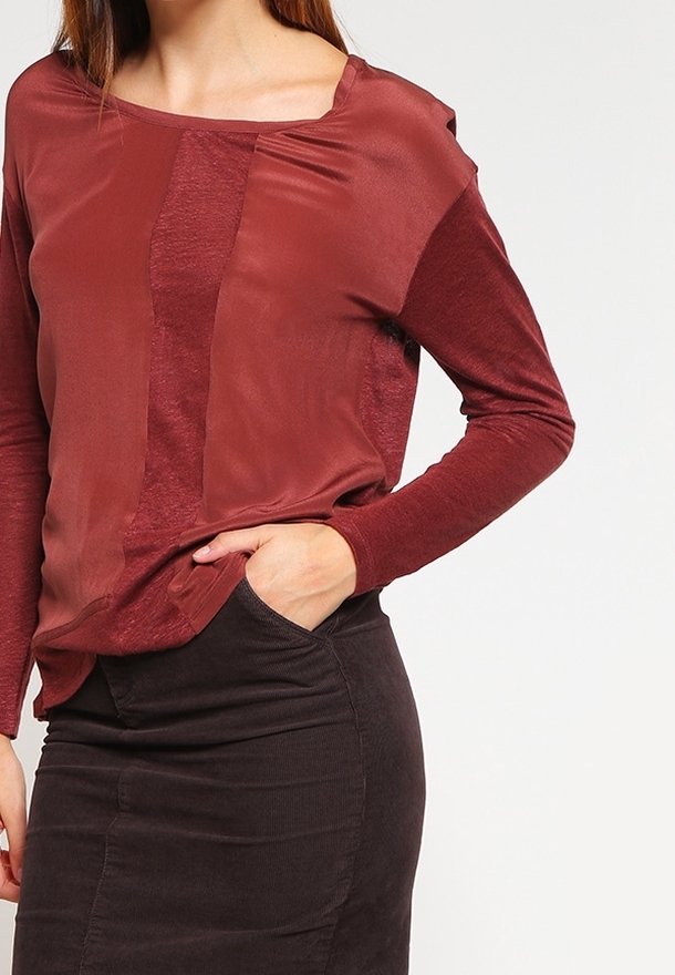 Top burdeos de manga larga con texturas variadas, que presenta un escote de pico y una mezcla de tejidos lisos y acanalados. Detalle de diseño sutil en las costuras.