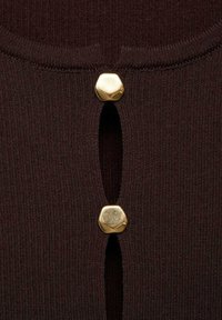 Bruin ribbelstof heeft twee gouden hexagonale knopen bij een opening, wat de textuur en ontwerpelementen benadrukt.