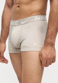 Torse masculin et partie supérieure des jambes portant un boxer Nike beige clair avec un logo visible sur la ceinture et la cuisse gauche.