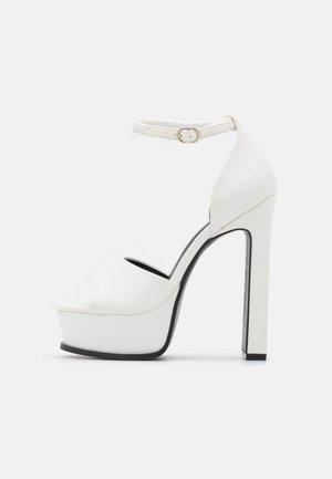 Hvide platform højhælede sandaler med ankelrem, glat lædertekstur, åben tå-design og sorte ydersålekonturer for godt greb.