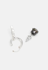 Brinco de argola prateado com um acabamento texturizado, combinado com um brinco de botão que apresenta um design de coroa preta e acentos metálicos.