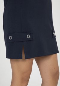 Marine jurk met een rechte snit, openingen aan beide zijden en twee stoffen stroken met metalen ogen voor detail. Soepele textuur.