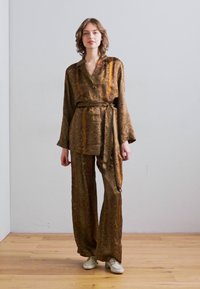 Completo due pezzi marrone a fantasia con una camicia con bottoni e pantaloni a gamba larga, dotato di una cintura da annodare e maniche lunghe, indossato con sneakers bianche.