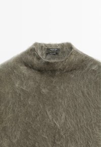Maglione in cashmere verde oliva con collo alto, texture morbida e un aspetto leggermente peloso, dotato di un'etichetta con dettagli sul marchio e sul materiale.