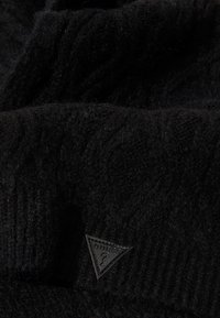 Berretto in maglia nera realizzato in morbida lana con un motivo testurizzato. Presenta una piccola etichetta a forma di triangolo nera con il logo "GUESS."
