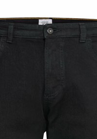 Sorte denimbukser med et klassisk fem-lommers design, knap- og lynlåslukning, med kontrasterende syninger og et mærke indeni taljen.