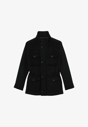 Juodas, su sagomis užsegamas paltas su aukštu apykakliu, dviem krūtinės kišenėmis ir šoninėmis kišenėmis. Turi tiesų kirpimą ir lygią audinio tekstūrą.