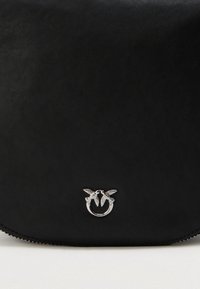 Μαύρη δερμάτινη τσάντα με ασημένια μεταλλική κούμπωμα που παρουσιάζει δύο λεπτομερή πουλιά που κοιτάζονται, με τις φτερούγες ανοιχτές, σχηματίζοντας έναν κυκλικό σχήμα.