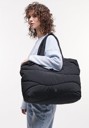 Schwarze gepolsterte Tragetasche mit einem gesteppten Design, ausgestattet mit breiten Trägern und einem Logo auf der Vorderseite. Über die Schulter getragen.