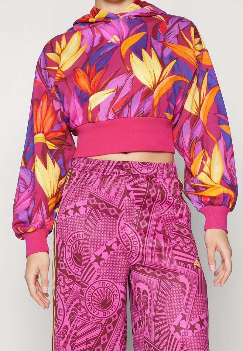 Lila huvtröja med blommönster, har långa puffärmar och ett rosa band; kombinerad med rosa mönstrade byxor, elastisk midja.