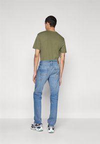 Tricou verde măsliniu cu mânecă scurtă, asortat cu blugi deschiși la culoare, cu croială dreaptă și design clasic cu cinci buzunare. Adidași albaștri și negri.