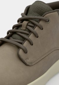 Bruine leren sneakers met een mesh-tong, contrasterende veters, ton-sur-ton stiksels en een gladde, gestructureerde afwerking op de bovenkant.