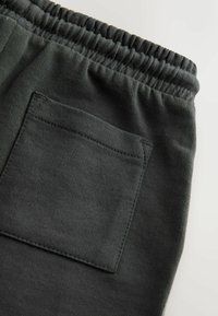 Pantaloni de trening gri închis cu talie nervurată, având un buzunar pătrat aplicat pe lateral și o finisare moale, cu textură plăcută a țesăturii.