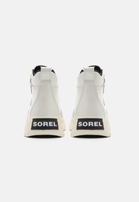 Zapatillas altas blancas con un acabado texturizado, que presentan un logo negro de SOREL en la parte trasera. Suela de goma redondeada y diseño minimalista.
