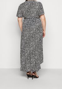 Sukienka maxi z lekkiej tkaniny w czarno-biały cętkowany wzór, z krótkimi rękawami i taliowanym krojem. Czarne sznurowane szpilki.