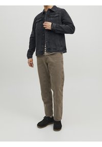 Black denim jacket with front pockets, worn over a striped shirt. Beige corduroy pants feature visible stitching and side pockets. Black boots.