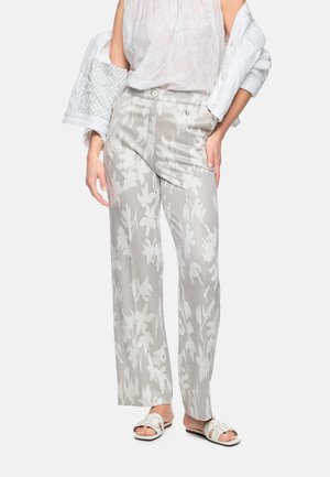 Woman wearing light gray floral wide-leg pants, white sleeveless blouse, white jacket off shoulders, and white sandals.