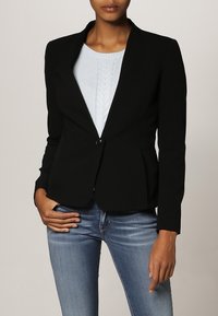 Svart skräddarsydd kavaj med en knappstängning, slim fit och spetsig krage, kombinerad med en ljusblå texturerad tröja under.