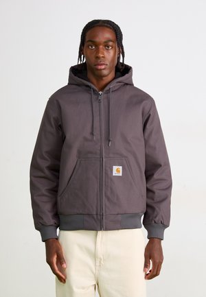 Gray zip-up hoodie with a lined hood, front pocket, and ribbed cuffs. Features a small orange Carhartt logo patch on the left pocket.