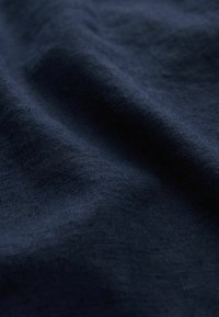 Teksturowana tkanina w kolorze granatowym o miękkim, naturalnym wykończeniu, z subtelnymi różnicami w splocie i głębi, tworząca dynamiczny efekt wizualny.