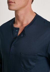 Navyblauwe henley-shirt van gladde stof, met een knoopsluiting op de kraag, een zak en kleurrijke patroonaccenten onder de halslijn.