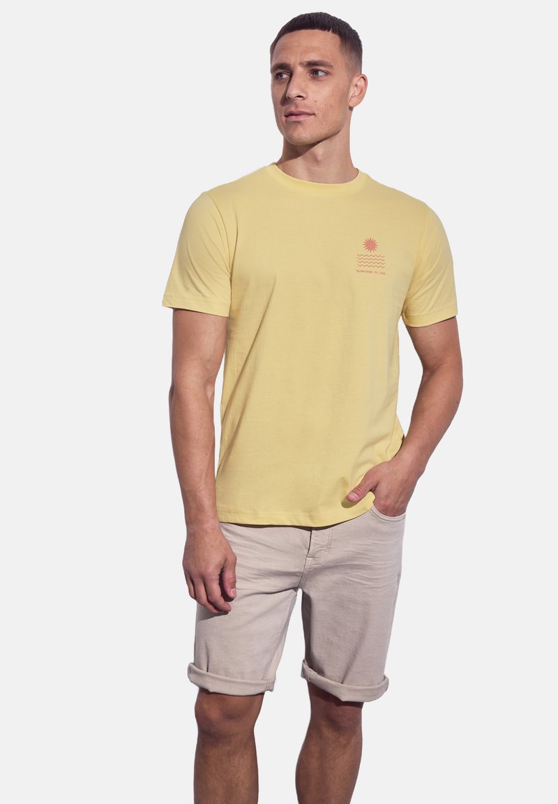 Žluté bavlněné tričko s krátkým rukávem a kulatým výstřihem, s malou grafikou slunce a vlny v červené barvě na levé straně hrudníku.