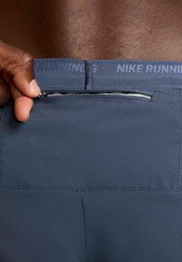 Pantalones cortos deportivos de color azul oscuro con una tela texturizada, que cuentan con un bolsillo con cremallera en la parte trasera y "NIKE RUNNING" grabado en la cintura.
