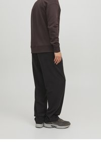 Felpa marrone scuro con polsini e orlo a coste, abbinata a pantaloni neri larghi. Sneakers grigie completano l'outfit.
