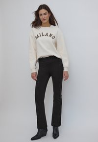 Sweat-shirt crème avec le texte "MILANO" en marron, associé à un pantalon noir ajusté et des bottines noires. Texture lisse, coupe décontractée.