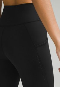 Leggings negre cu talie înaltă, dintr-un material fin, având o buzunar lateral și accente discrete de puncte de-a lungul cusăturii piciorului.
