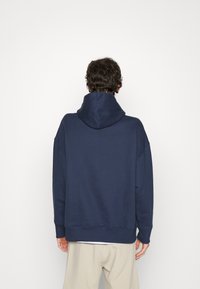 Felpa blu navy con un ampio cappuccio, vestibilità rilassata e polsini a coste. Realizzata in un tessuto morbido, presenta un design semplice senza loghi o motivi.