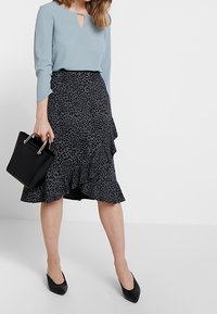 Světle modrá halenka s detaily ve tvaru klíčové díry, spárovaná s černou sukní s leopardím potiskem a volány. Černá kabelka a černé lodičky s špičatou špičkou dokončují celkový vzhled.