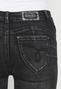 Jean en denim noir vu de dos montrant les coutures décoratives des poches et l’étiquette de la marque Koroshi sur la ceinture.