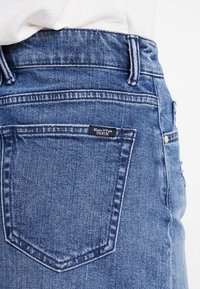 Mörkblå denimjeans med hög midja, som har en bakficka med en sydd kant och en svart etikett med texten "Marc O'Polo DENIM."
