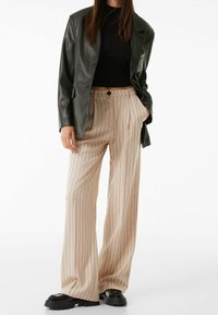 Mörkgrön läderblazer, svart ribbad topp, beige randiga vida byxor med knäppning och klumpiga svarta skor.