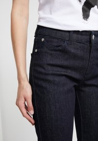 Jeans de mezclilla azul oscuro con un corte recto, diseño de cinco bolsillos, detalles de costura sutiles y herrajes metálicos plateados en los bolsillos.