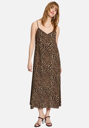 Mujer con un vestido sin mangas, con estampado de leopardo hasta los tobillos, con tirantes finos y sandalias negras de tacón alto sobre un fondo liso.