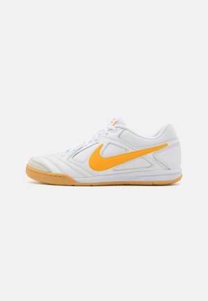 Fehér sportcipő narancssárga kiegészítőkkel, texturált szintetikus felsőrész, fehér fűzők, párnázott talp és jellegzetes Nike logó.