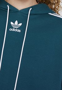 Teal hoodie med vit dragsko, sidostrimmor och broderad Adidas-logotyp med tre-randig detalj på bröstet.