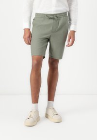 Shorts en coton vert pâle avec une taille élastique et un cordon de serrage. Comprend des poches latérales et une coupe simple et droite.