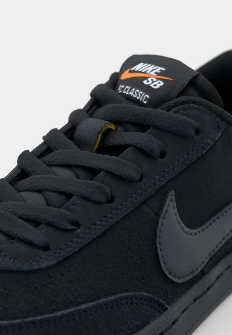 Schwarze Wildleder-Sneaker mit strukturiertem Finish, grauem Nike-Logo und passenden Schnürsenkeln; "NIKE SB CLASSIC"-Etikett auf der Zunge in Schwarz und Orange.