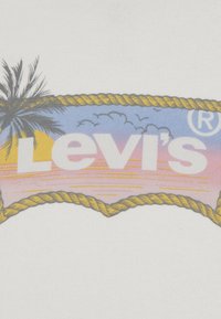 Tissu blanc avec un logo Levi's sur fond de coucher de soleil, palmiers et accents de corde jaune. Le design comprend des nuages et une marque déposée.