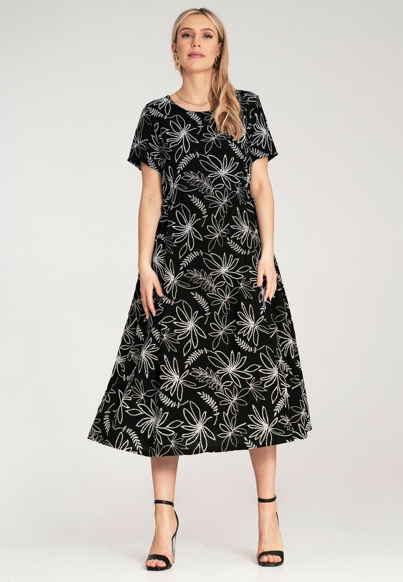 Black floral maxi dress with short sleeves, featuring white floral patterns. Made from soft fabric, flares at the hem, paired with strappy heels.