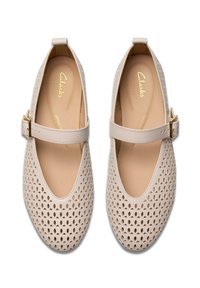 Zapatos beige de estilo Mary Jane, perforados, con una correa y detalle de hebilla. Presentan un forro interior suave y un diseño de punta redondeada.