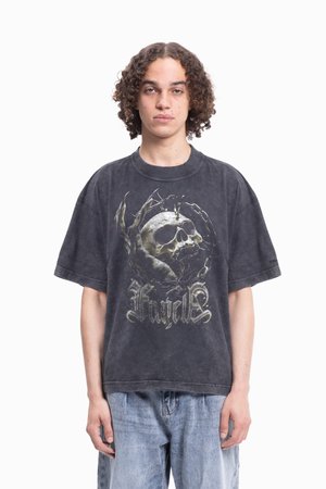 Ung person med lockigt hår som bär en urtvättad svart oversized T-shirt med en dödskalle- och klotågsgrafik samt ljusblå jeans.