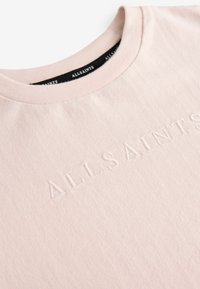 Gaiši rozā kokvilnas T-kreklis ar apaļu kakla izgriezumu, uz kura priekšpuses ir reljefs "ALLSAINTS" logos un melna kakla lente.