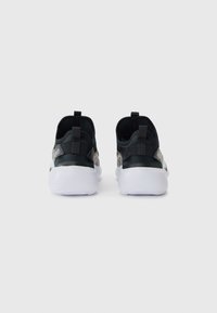 Des chaussures de sport noires avec une semelle blanche, présentant une texture lisse et des languettes à l'arrière pour un enfilage facile.