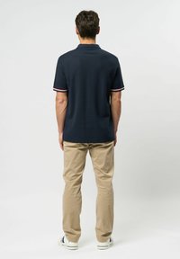 Navy polo-paita, jossa on kontrastiväriset punaiset ja valkoiset raidalliset hihansuut, yhdistettynä khaki-housuihin. Asusteina valkoiset lenkkarit raidallisilla yksityiskohdilla.