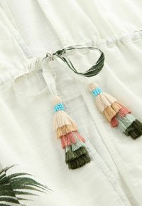 White fabric garment with a tie closure featuring tassels in shades of peach, green, and pink, accented with blue beads and leaf patterns.